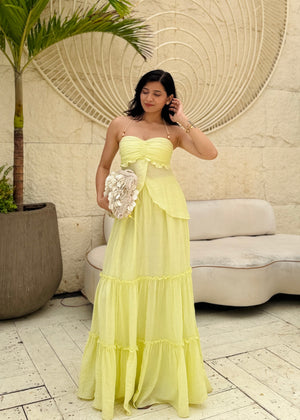 Woman in a yellow dress standing in front of a decorative wall with a palm tree and sofa in the background.