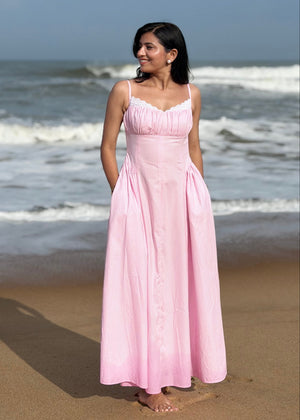 Woman in a pink dress standing on a beach with waves in the background
