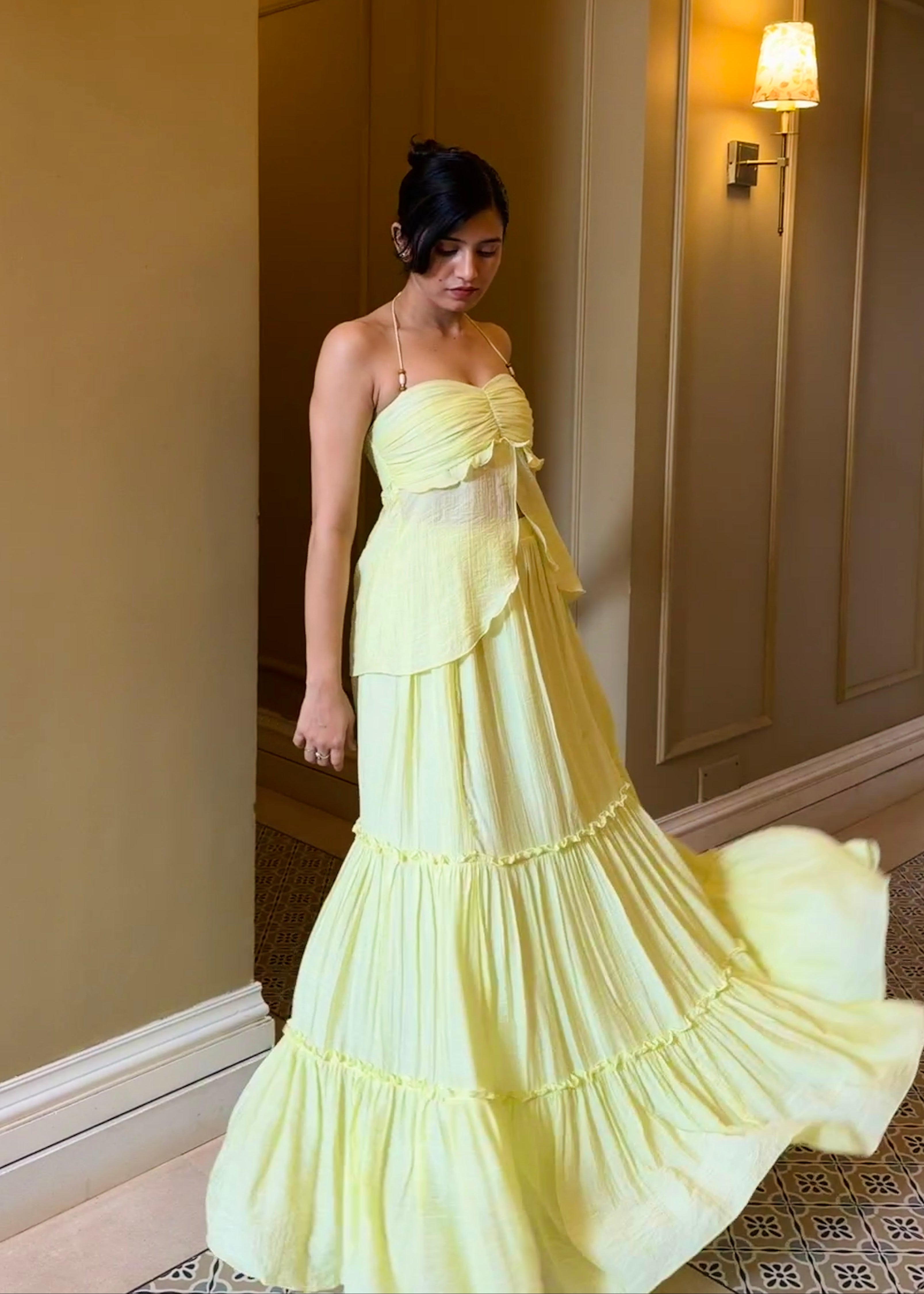 Woman in a yellow strapless gown standing in a room with beige walls and a lamp.