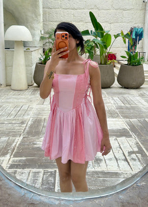Person wearing a pink dress taking a mirror selfie in an outdoor setting with plants and architectural elements.