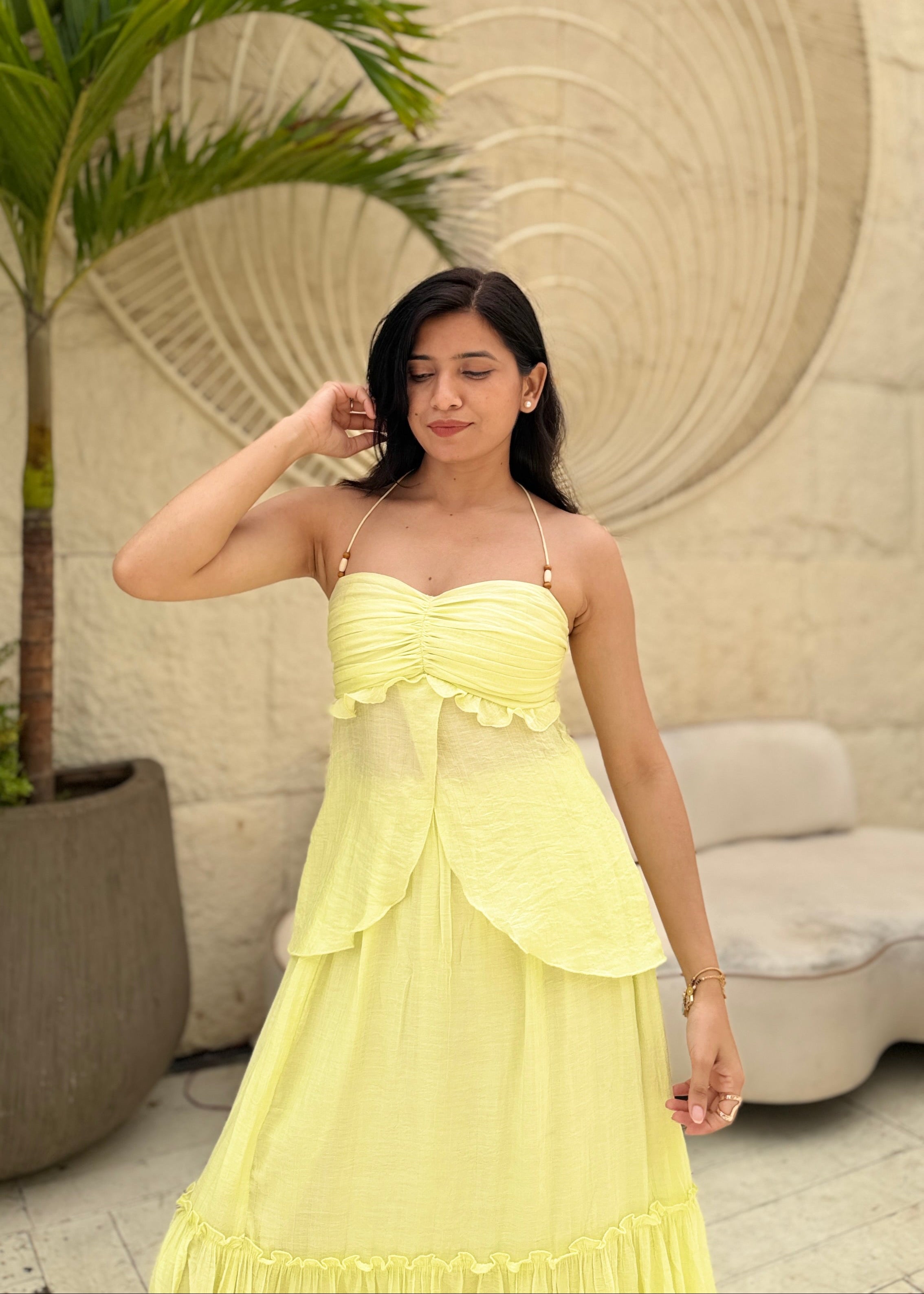 Woman in a yellow dress standing in front of a decorative wall and plant.