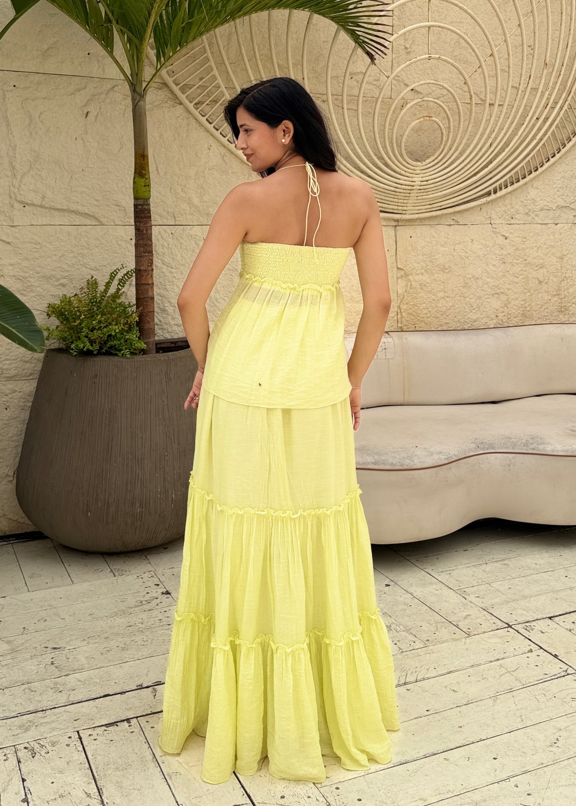 Woman in a yellow dress standing in a room with a decorative wall and plant.