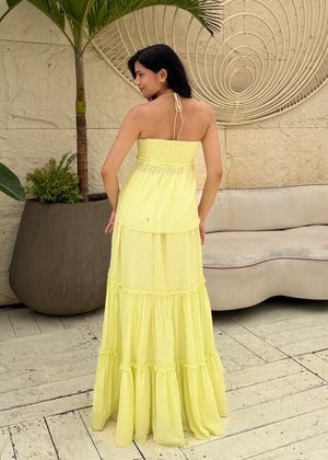 Woman in a yellow dress standing in a room with a decorative wall and plant.
