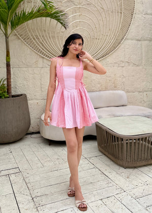 Woman in a pink dress standing in an outdoor setting with a textured wall and palm tree.