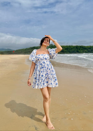 Woman in a floral dress standing on a beach with ocean and sky in the background