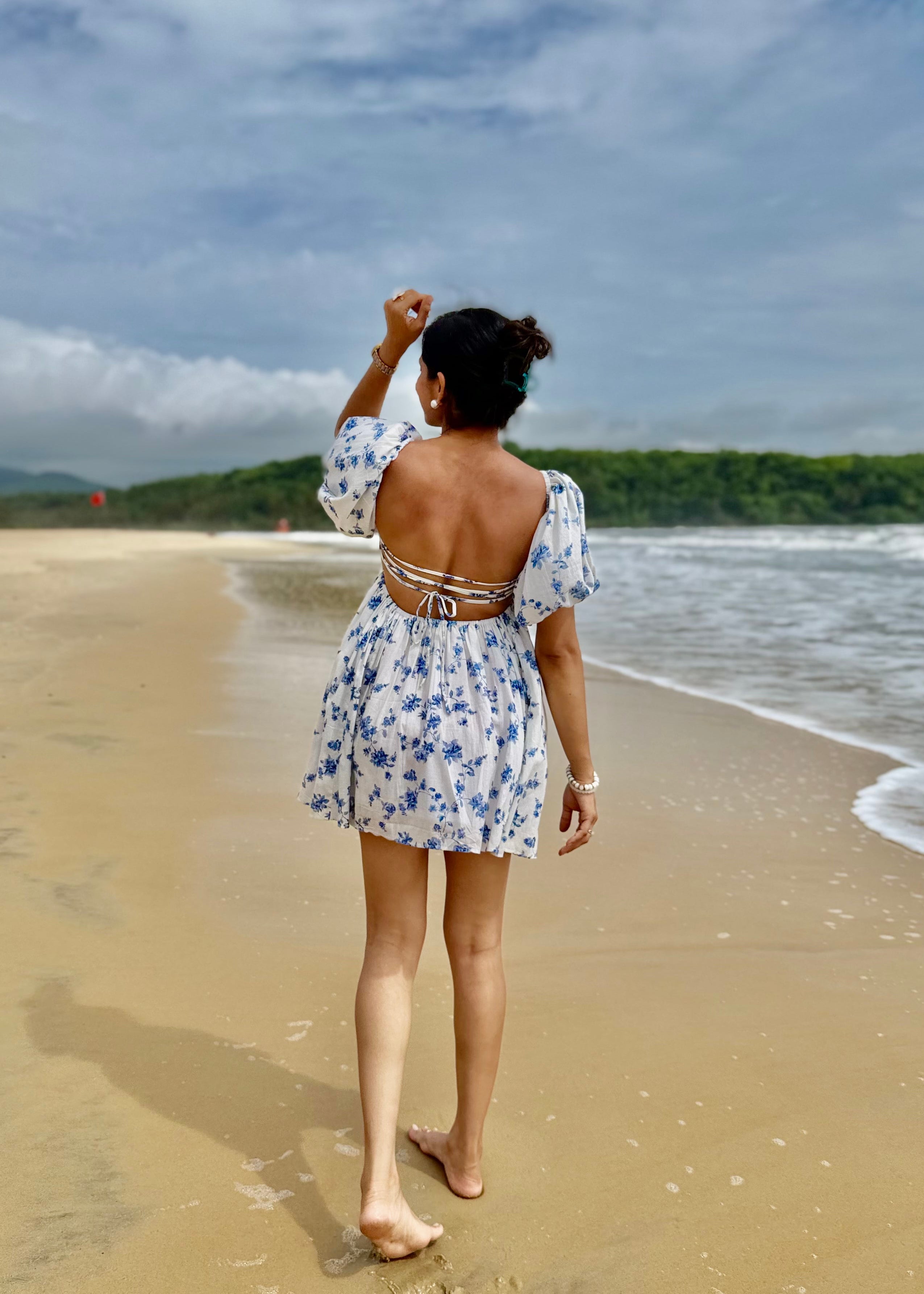 Woman in a floral dress standing on a beach with ocean and sky in the background