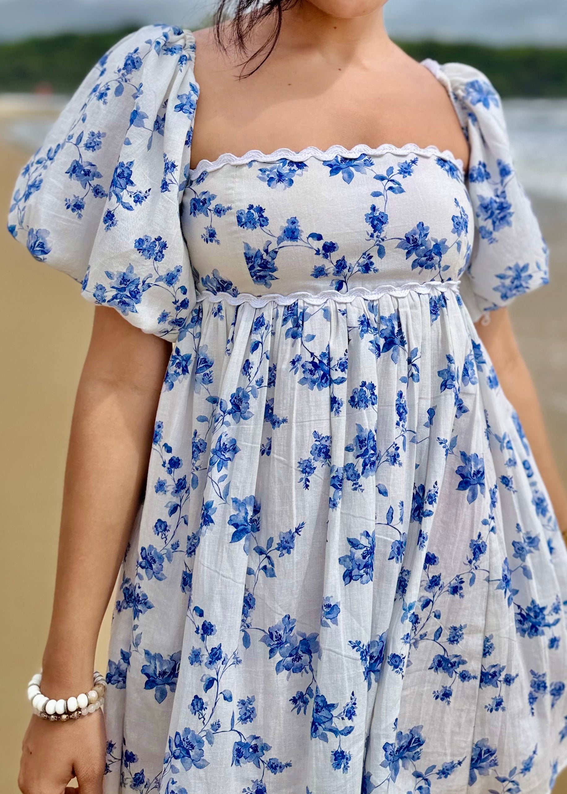 Woman in a blue and white floral dress standing on a beach.