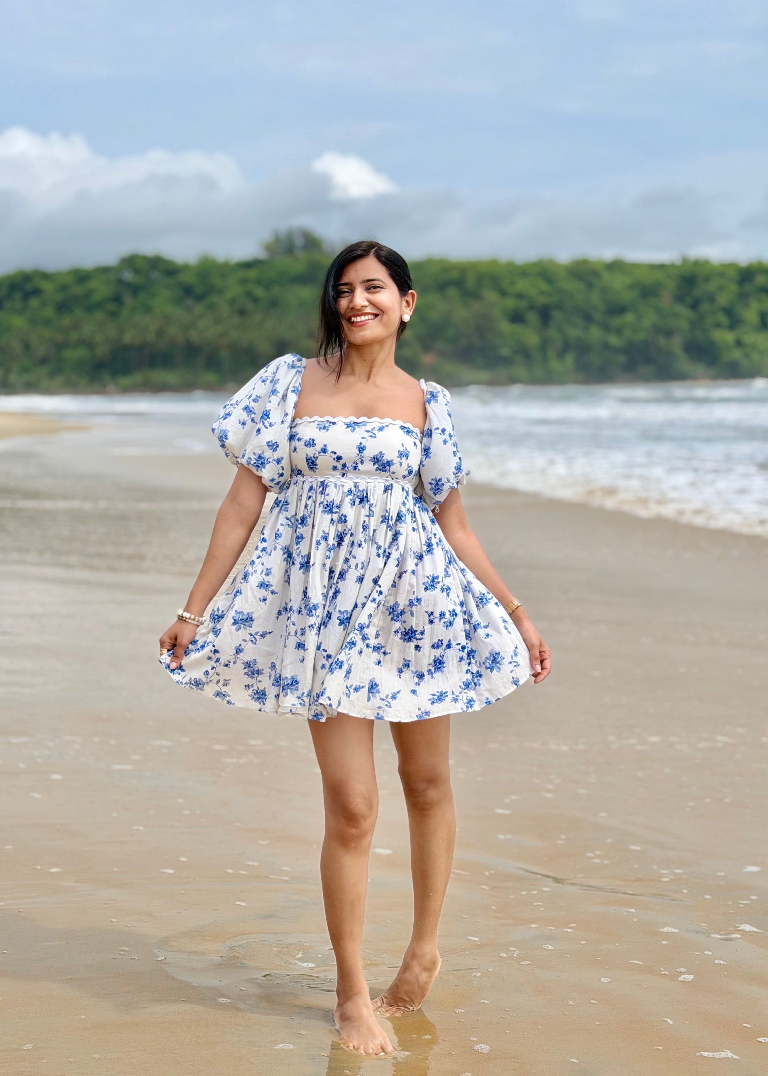 Woman in a floral dress standing on a beach with greenery in the background