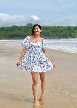 Woman in a floral dress standing on a beach with greenery in the background