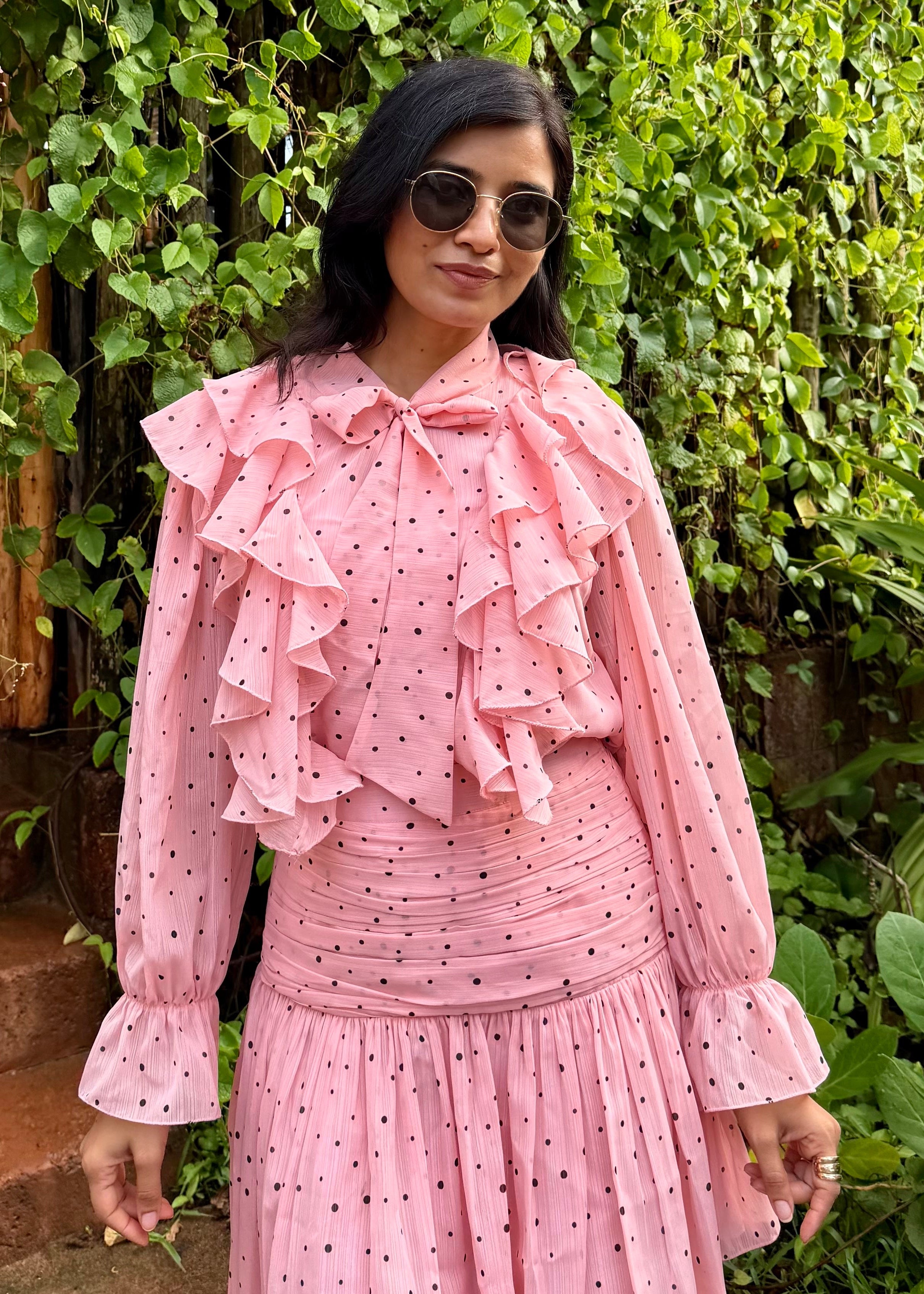 Woman in a pink dress standing in front of a green leafy wall.