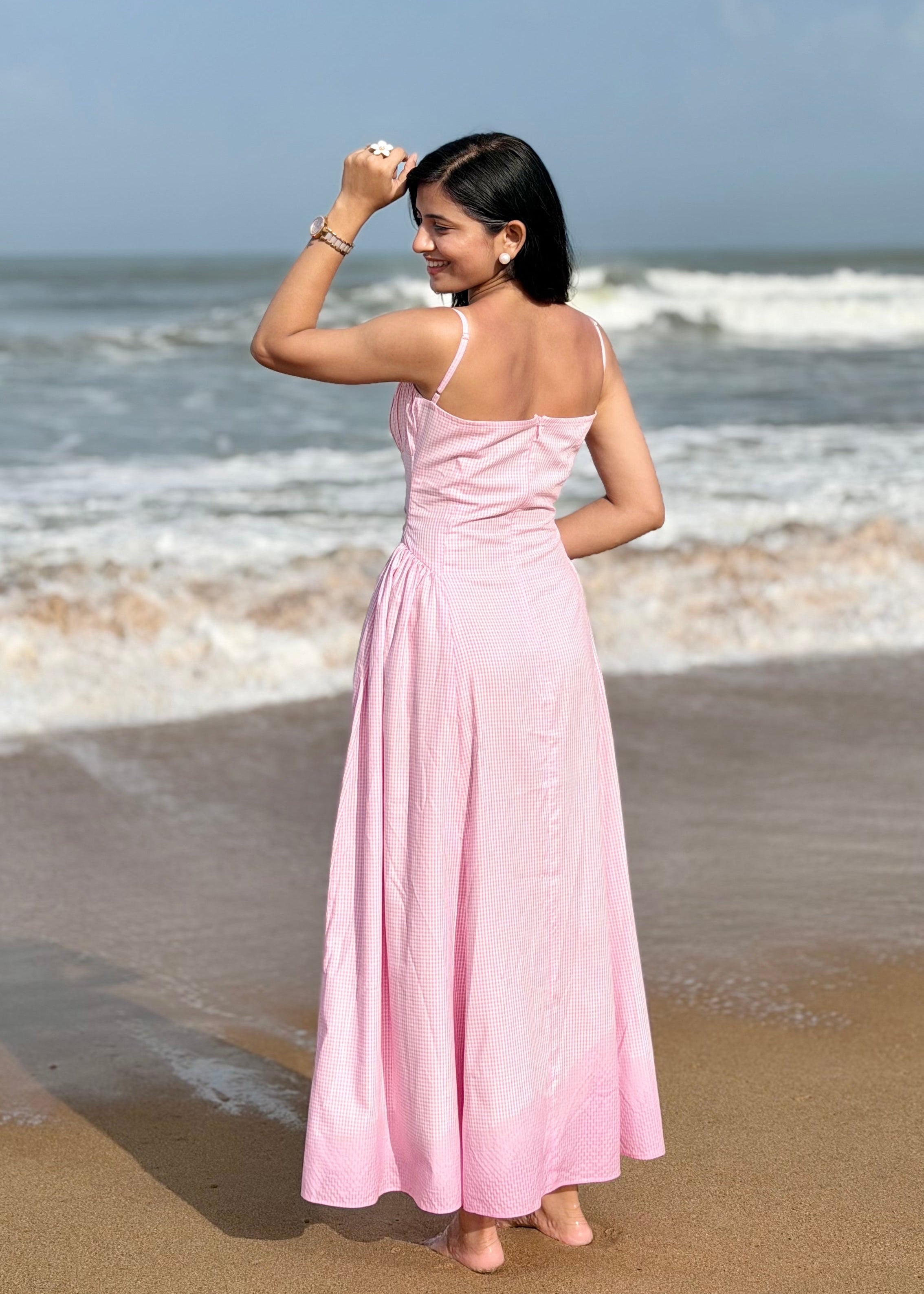 Woman in a pink dress standing on a beach with ocean waves in the background