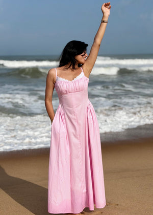 Woman in a pink dress standing on a beach with ocean waves in the background